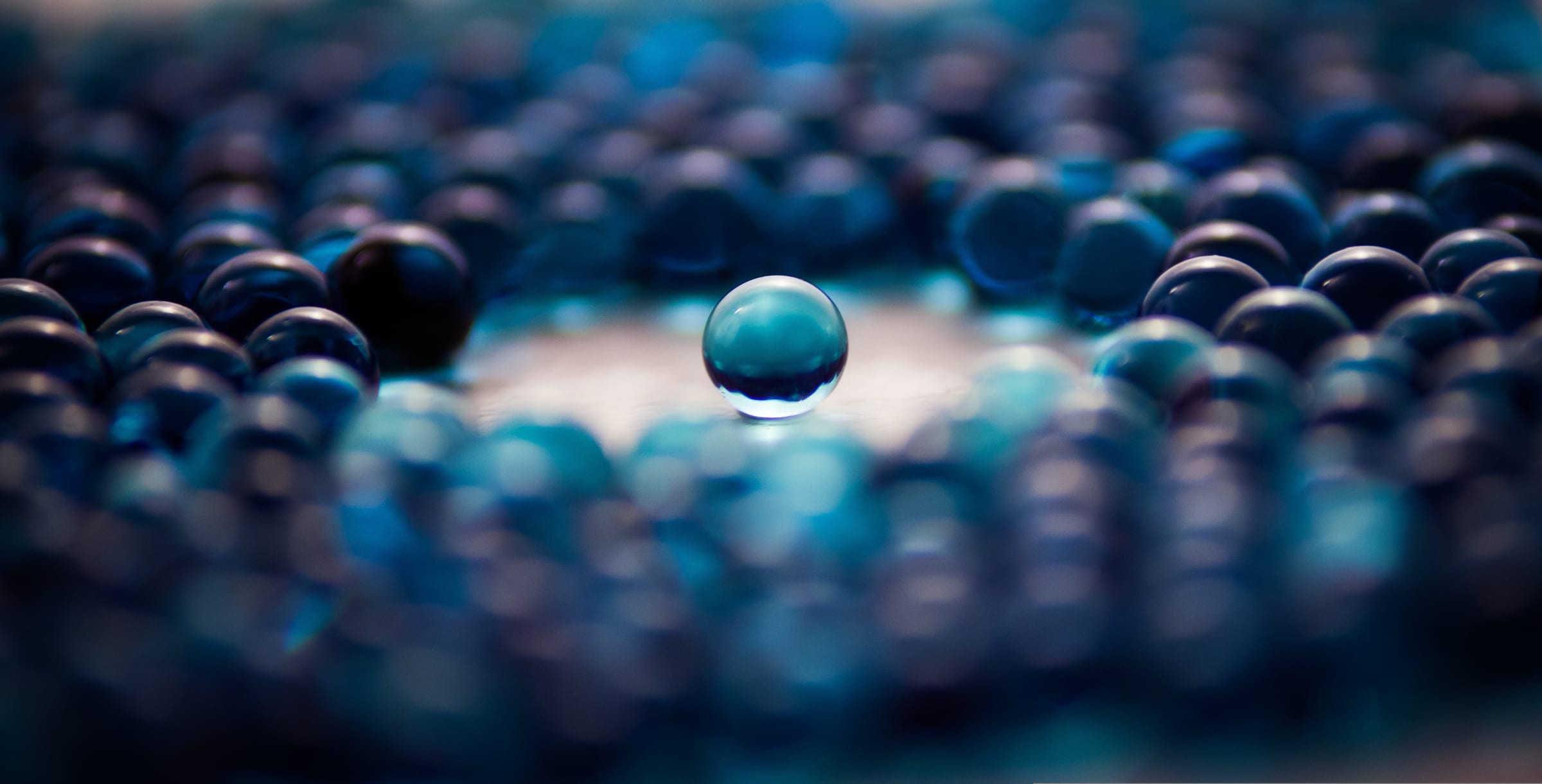 Eine einzelne, klare Glaskugel schwebt über einem Feld vieler blauer Kugeln - Sinnbild für eine zentrale Datenquelle inmitten vieler angebundener Systeme